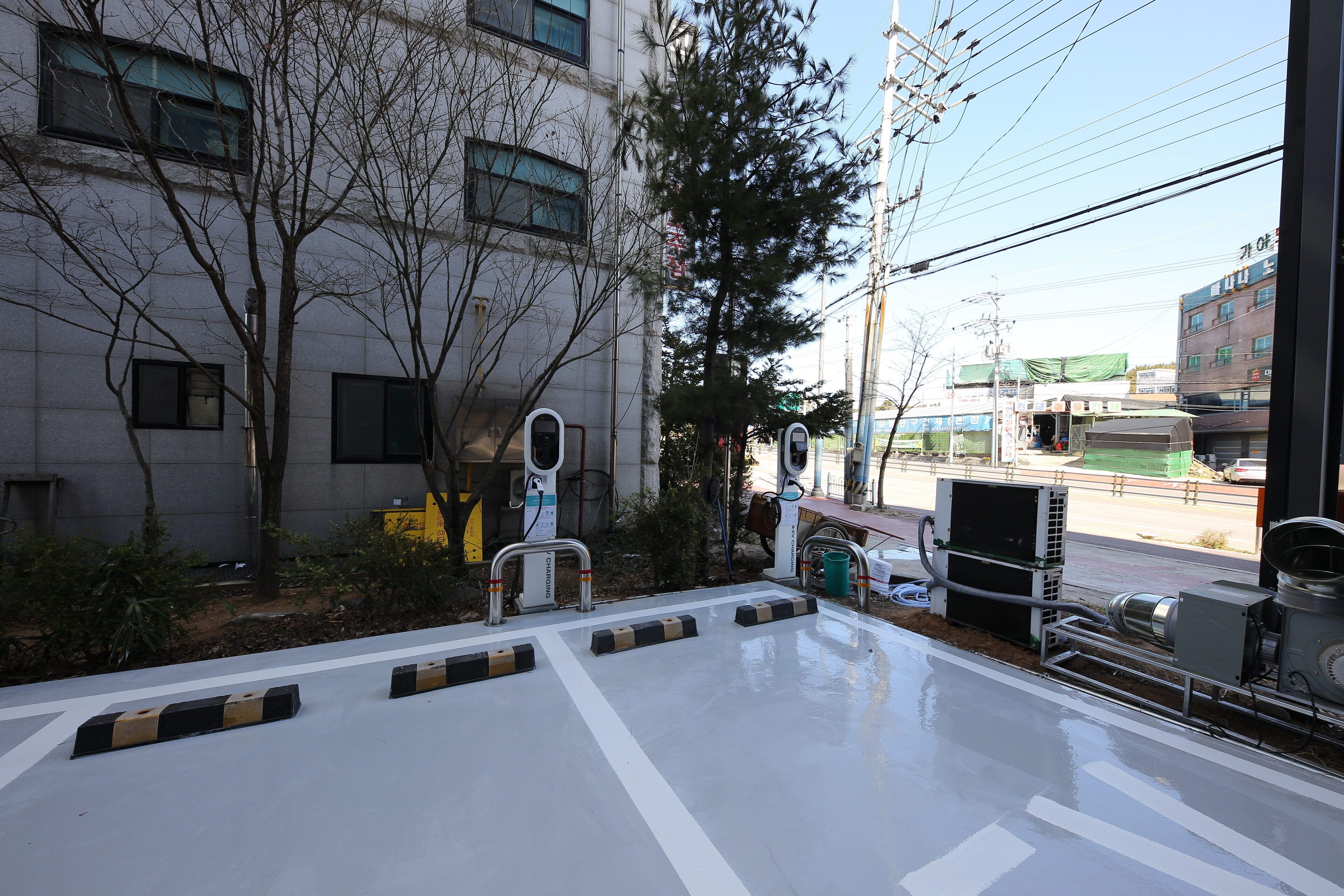 A view from a window overlooking a street with a building, trees, and parked vehicles.