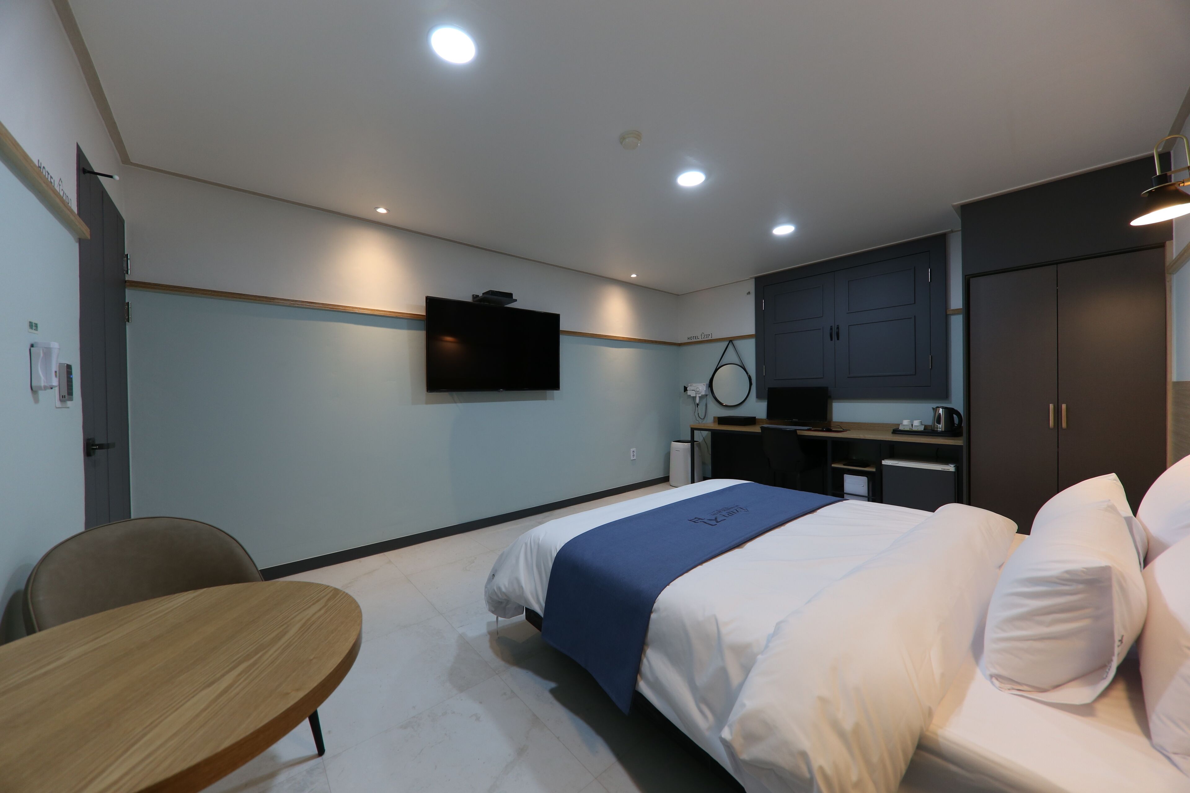 Quarto de hotel com cama, escrivaninha, cadeira, televisão e cozinha compacta.