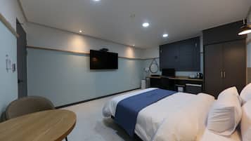 Quarto de hotel com cama, escrivaninha, cadeira, televisão e cozinha compacta.
