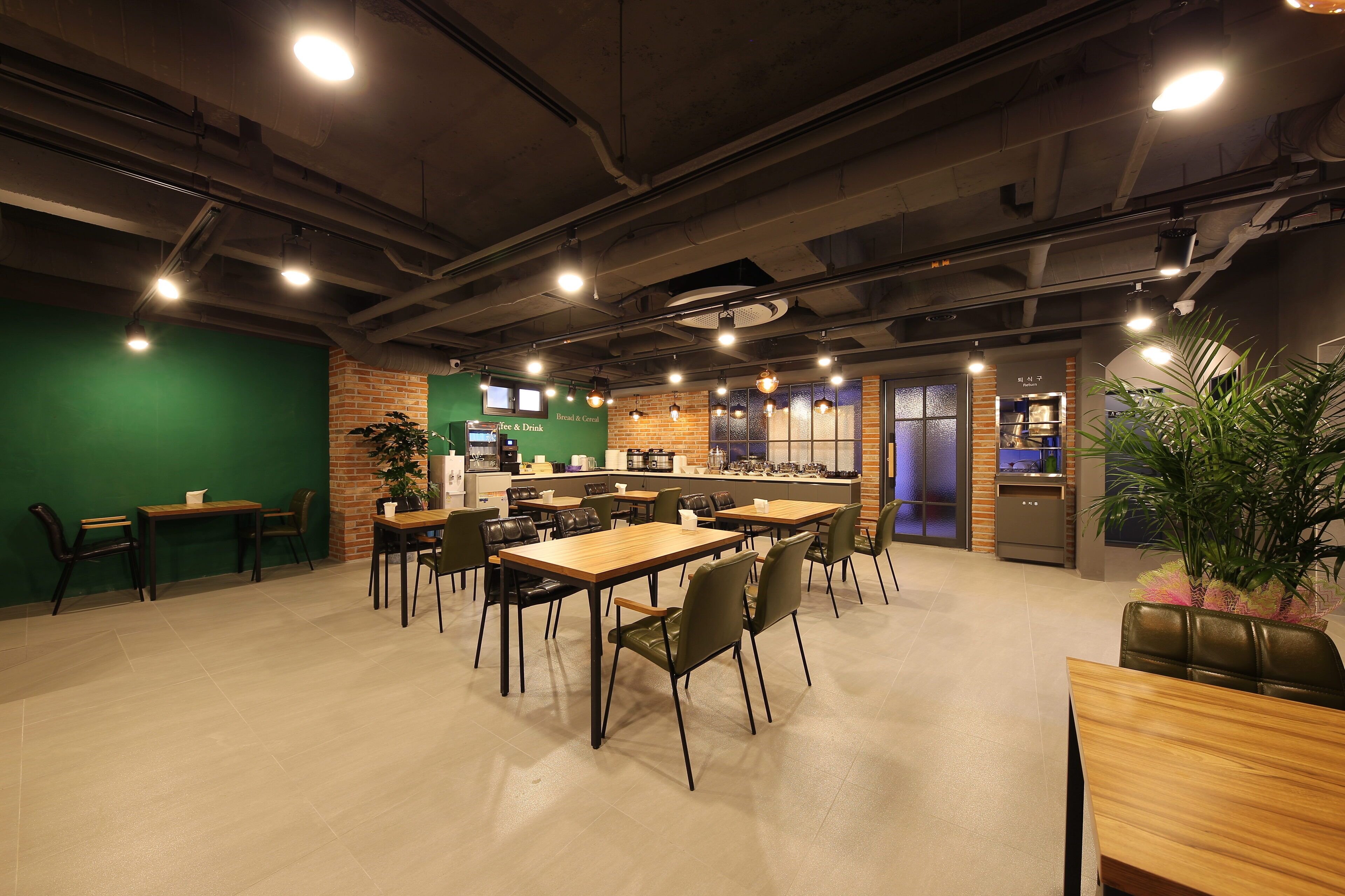 Un café moderno con varias mesas y sillas, una máquina de café y una pared verde.
