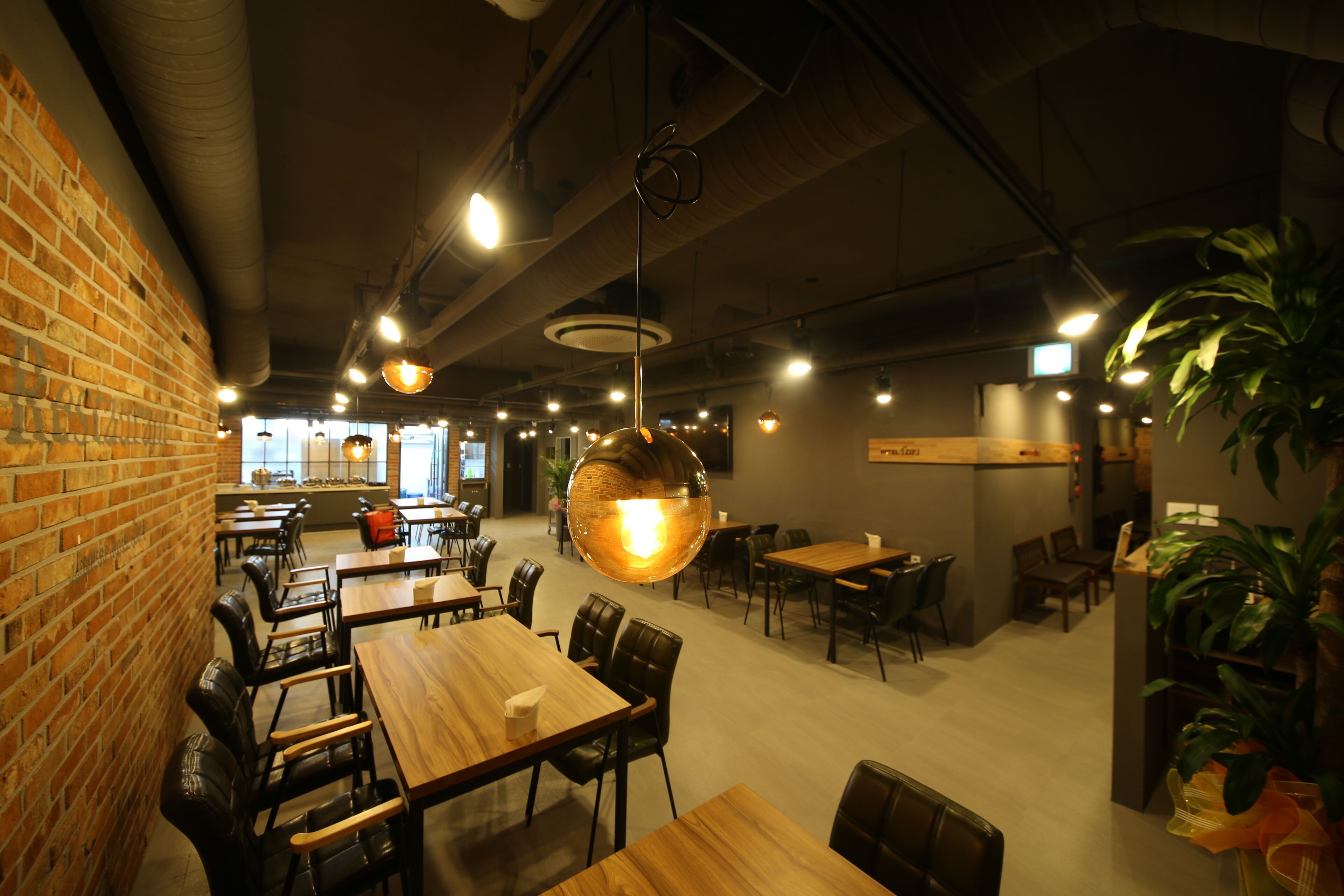 A spacious restaurant with brick walls, wooden tables, and hanging pendant lights.