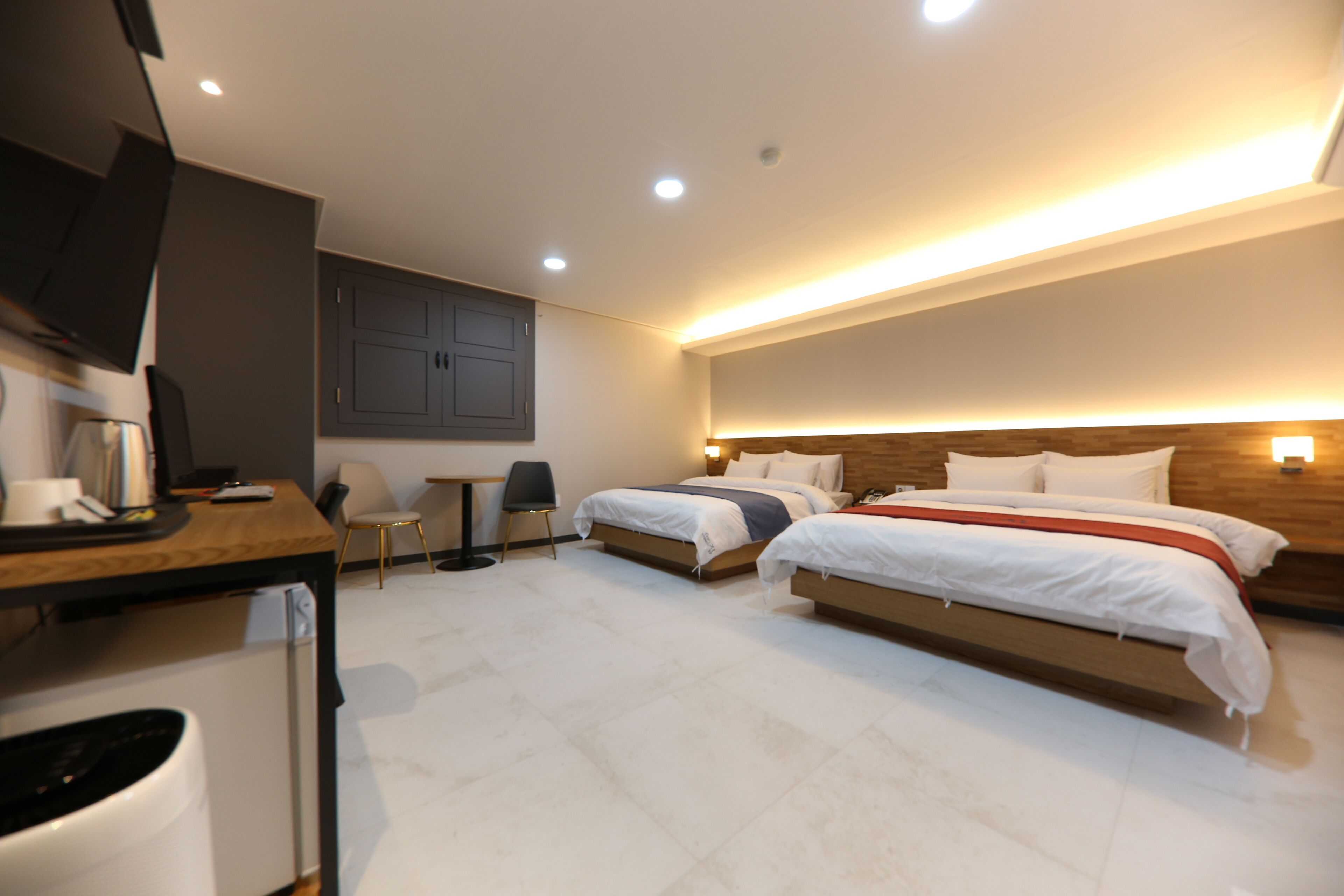 A modern hotel room with two beds, a desk, a chair, a television, and a small table.