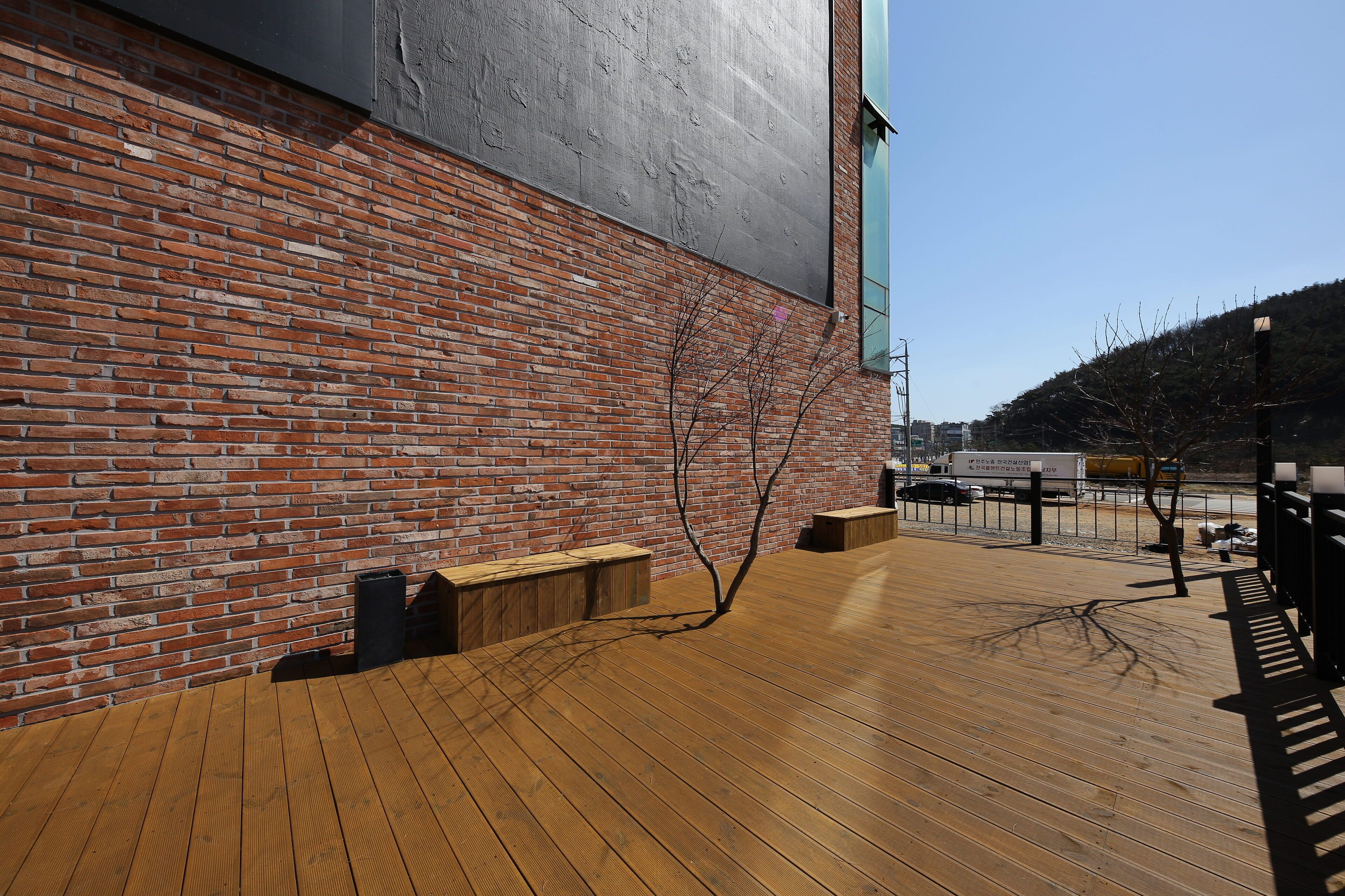 A wooden deck with benches, a brick wall, and a metal structure.