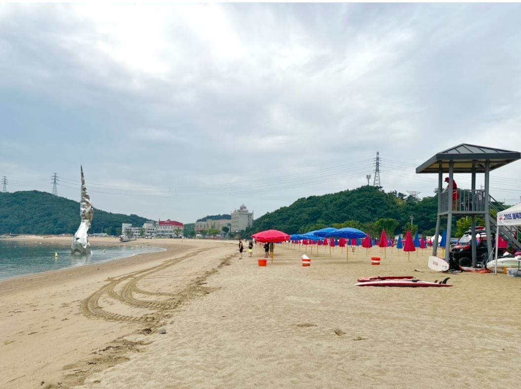 Una playa con sombrillas, una torre de salvavidas y una estatua.