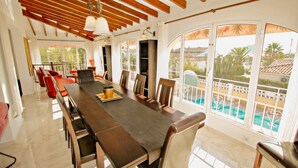 Une salle à manger spacieuse avec une longue table en bois, des chaises confortables et de grandes fenêtres donnant sur une piscine et un espace verdoyant.