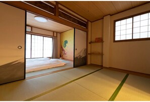 A traditional Japanese room with tatami flooring, sliding doors, and a bed with a mountain painting.