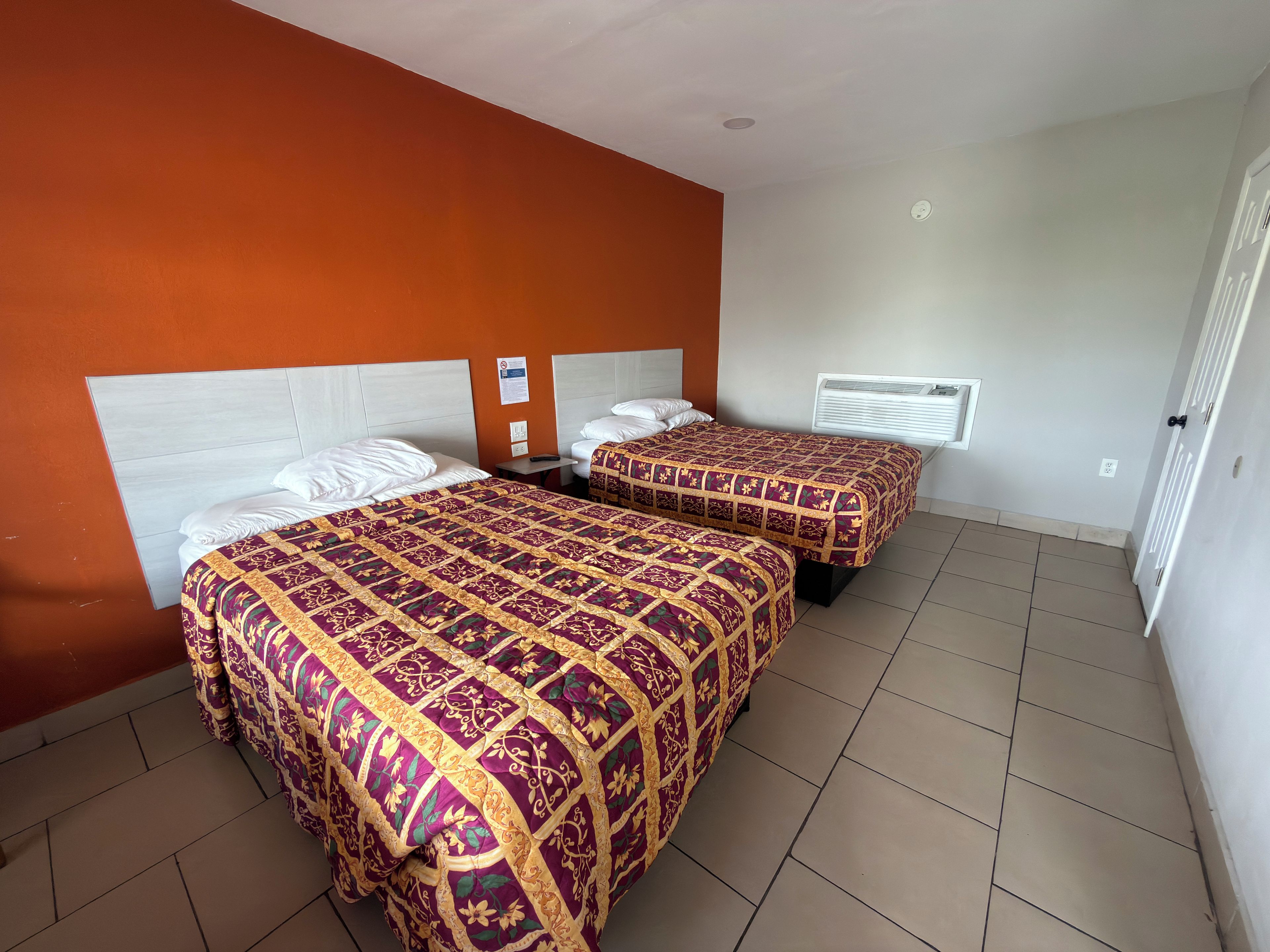 A hotel room with two beds, a white ceiling, and a window with blinds.