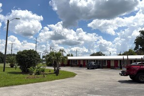 A building with a parking lot, a red vehicle, and a clear sky with clouds. - Tropicana Motel Wauchula FL (Wauchula)