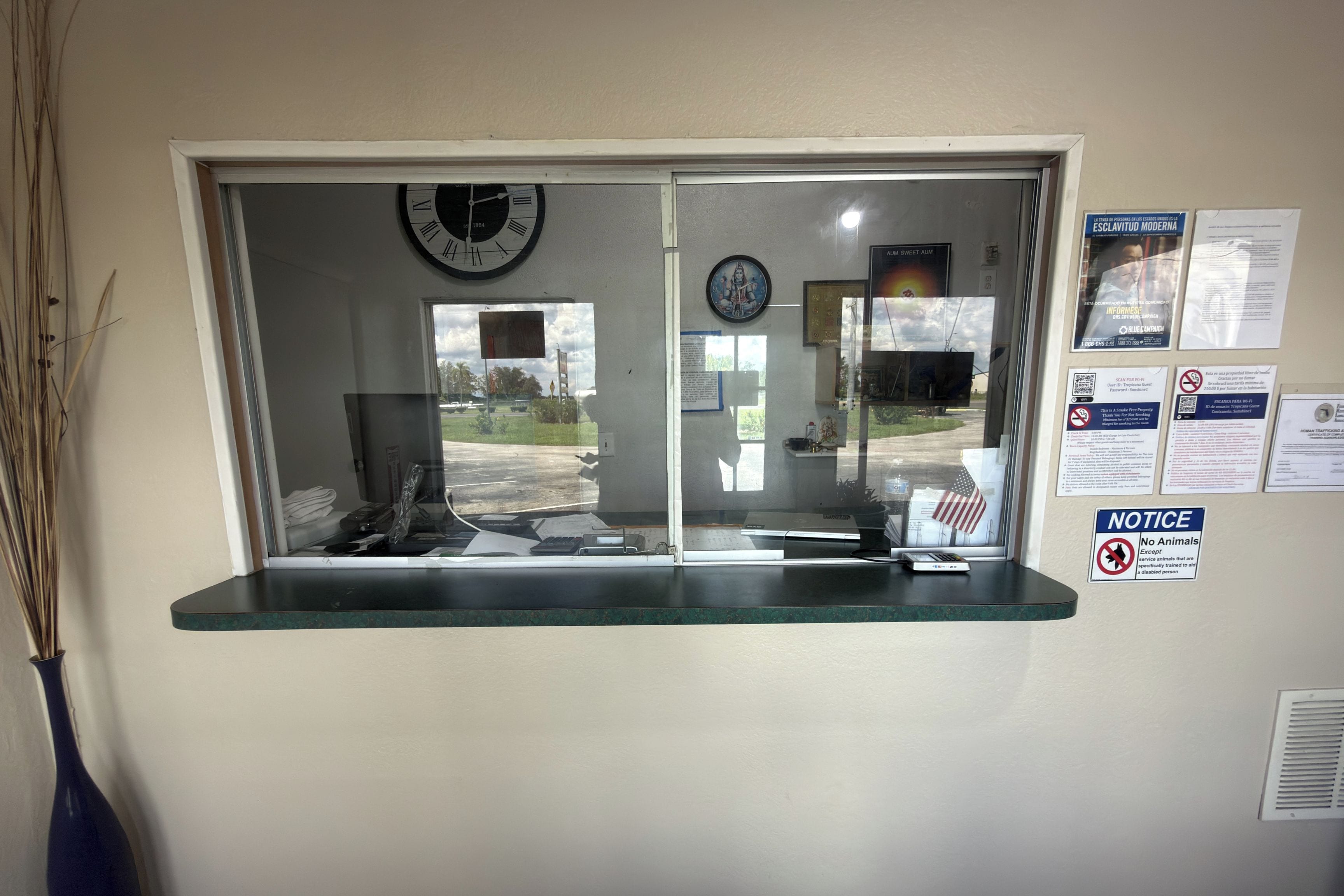 A reception desk with a clock, a window with a view of the outside, and various notices on the wall.