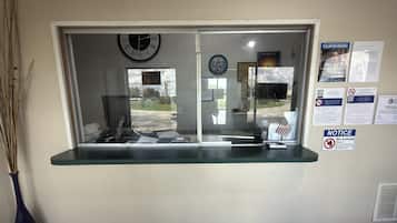 A reception desk with a clock, a window with a view of the outside, and various notices on the wall.