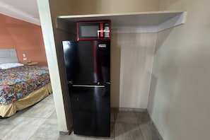 A compact black refrigerator with a microwave on top, positioned against a wall in a room with a bed and a colorful bedspread. - Tropicana Motel Wauchula FL (Wauchula)