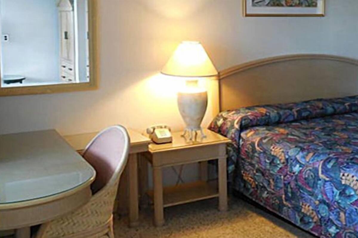 A hotel room with a bed, a desk with a lamp, a chair, and a small table.