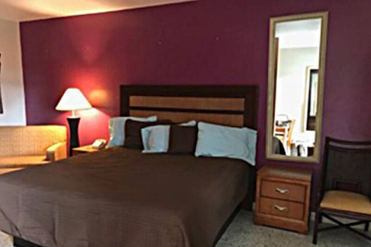 A hotel room with a bed, a nightstand, a lamp, a chair, and a dresser.