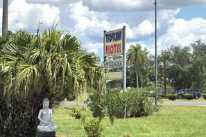 Skilt for Tropicana Motel med en Buddha-statue og vegetation i forgrunden.