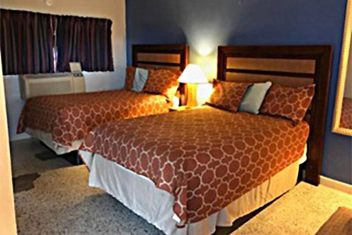 A hotel room with two beds, a nightstand, a lamp, and a window with curtains.