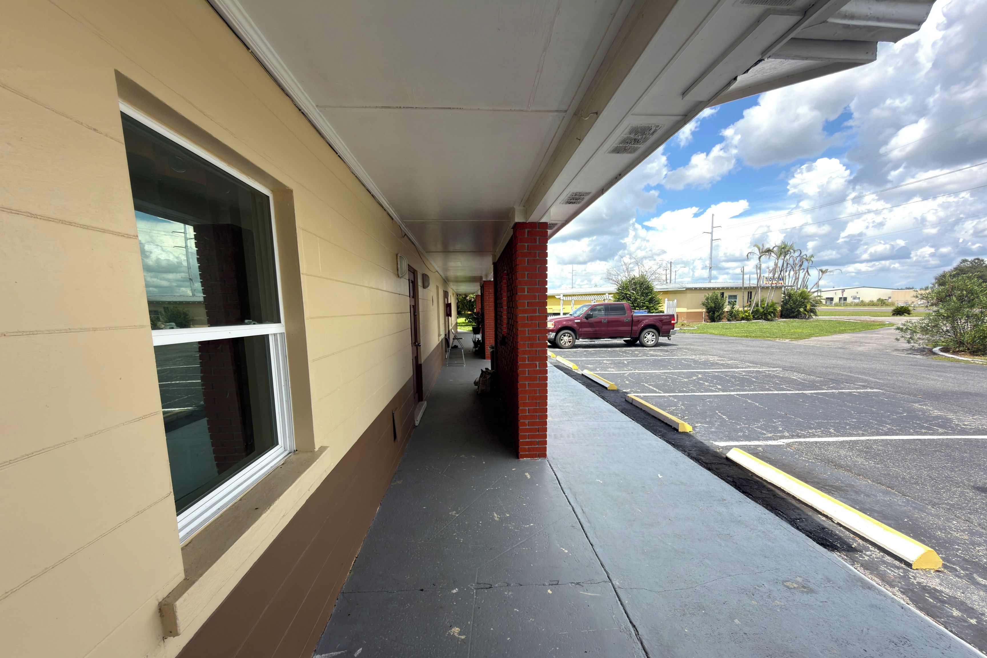 A covered walkway leading to a building with a large window and a parking lot in the background.