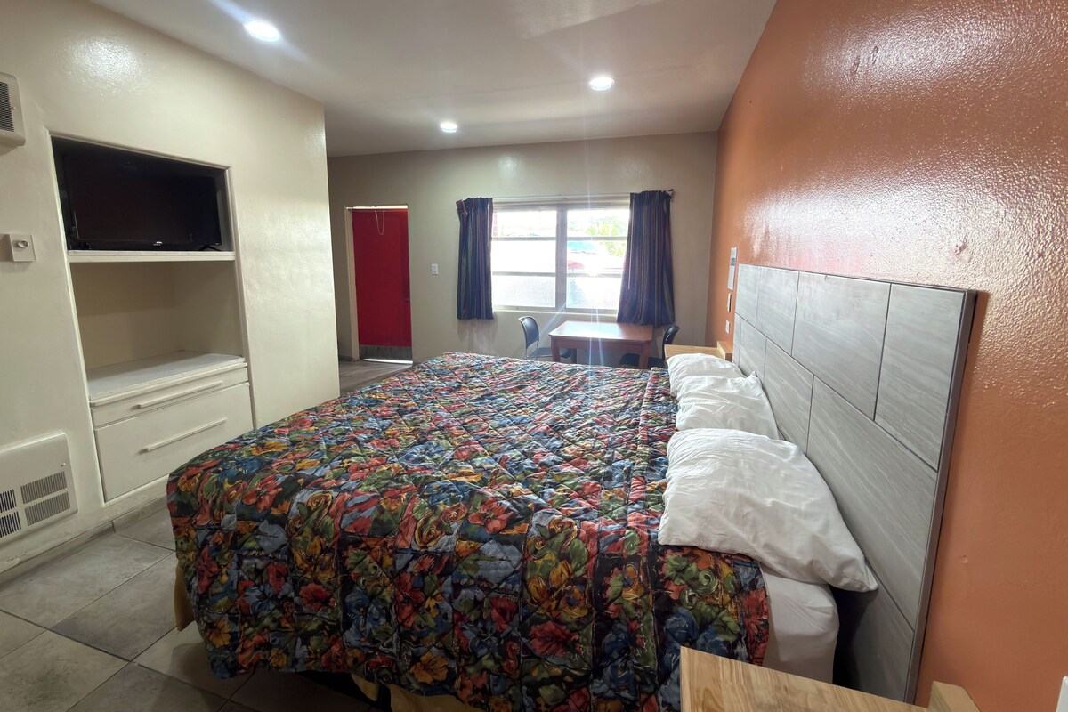 A hotel room with a bed, a TV, a desk, and a window with curtains.