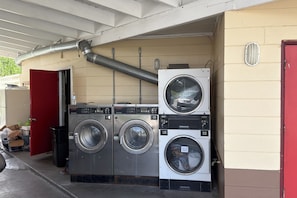 A laundromat with two stacked front-loading washers and dryers, a red door, and a ventilation system above. - Tropicana Motel Wauchula FL (Wauchula)