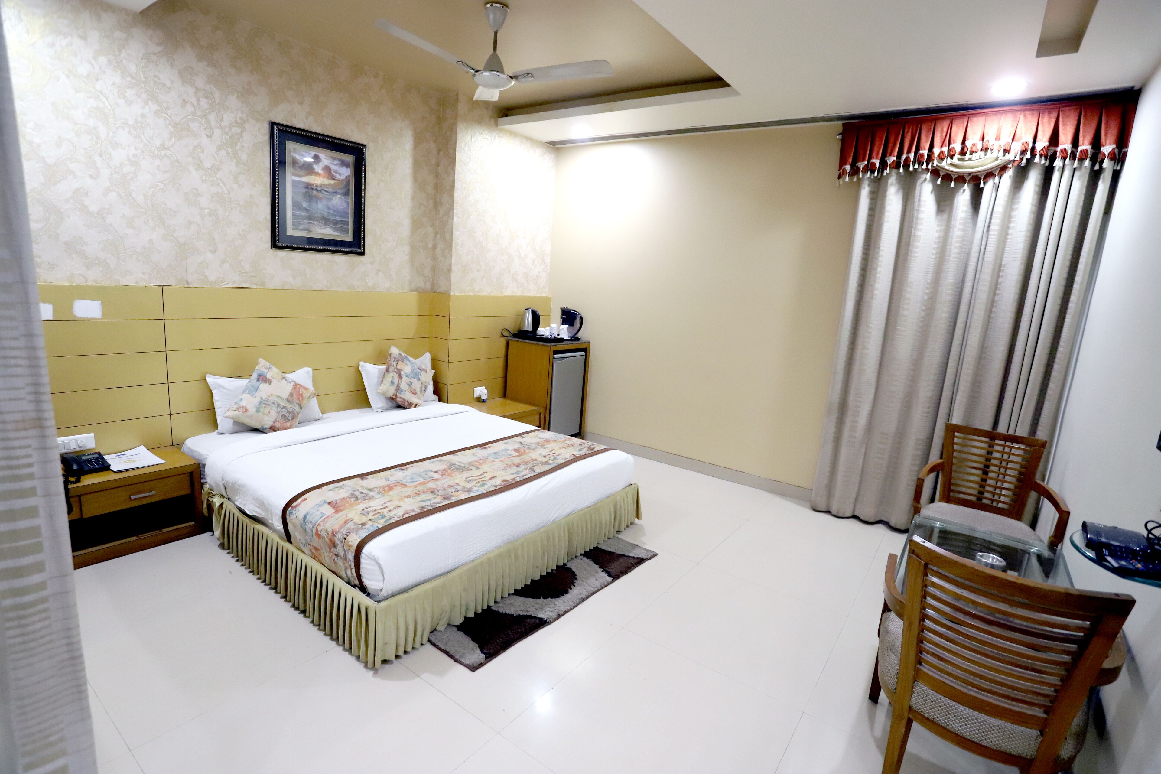 A hotel room with a bed, bedside table, nightstand, chair, and a desk with a chair.