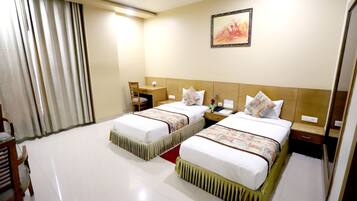 A hotel room with two beds, a desk, a chair, a nightstand, and a painting on the wall.
