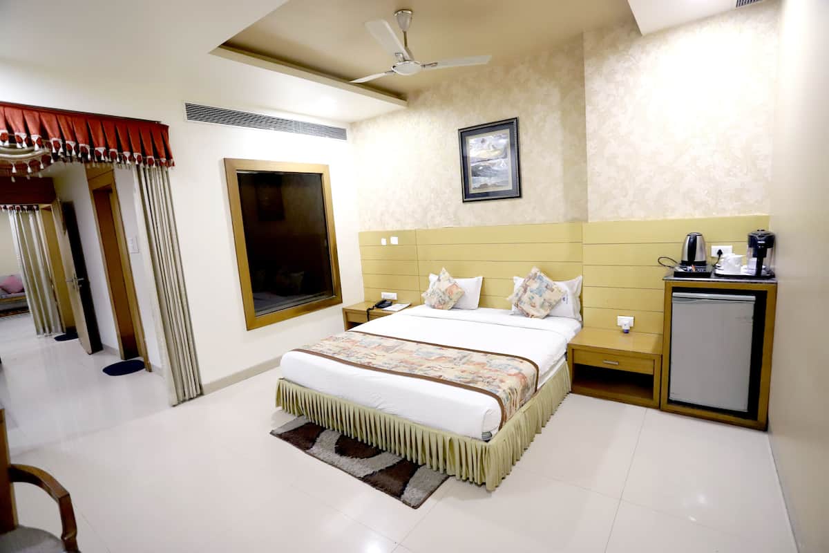 Quarto de hotel com cama, mesas de cabeceira, ventoinha no teto, mini-geladeira e janela com cortinas.