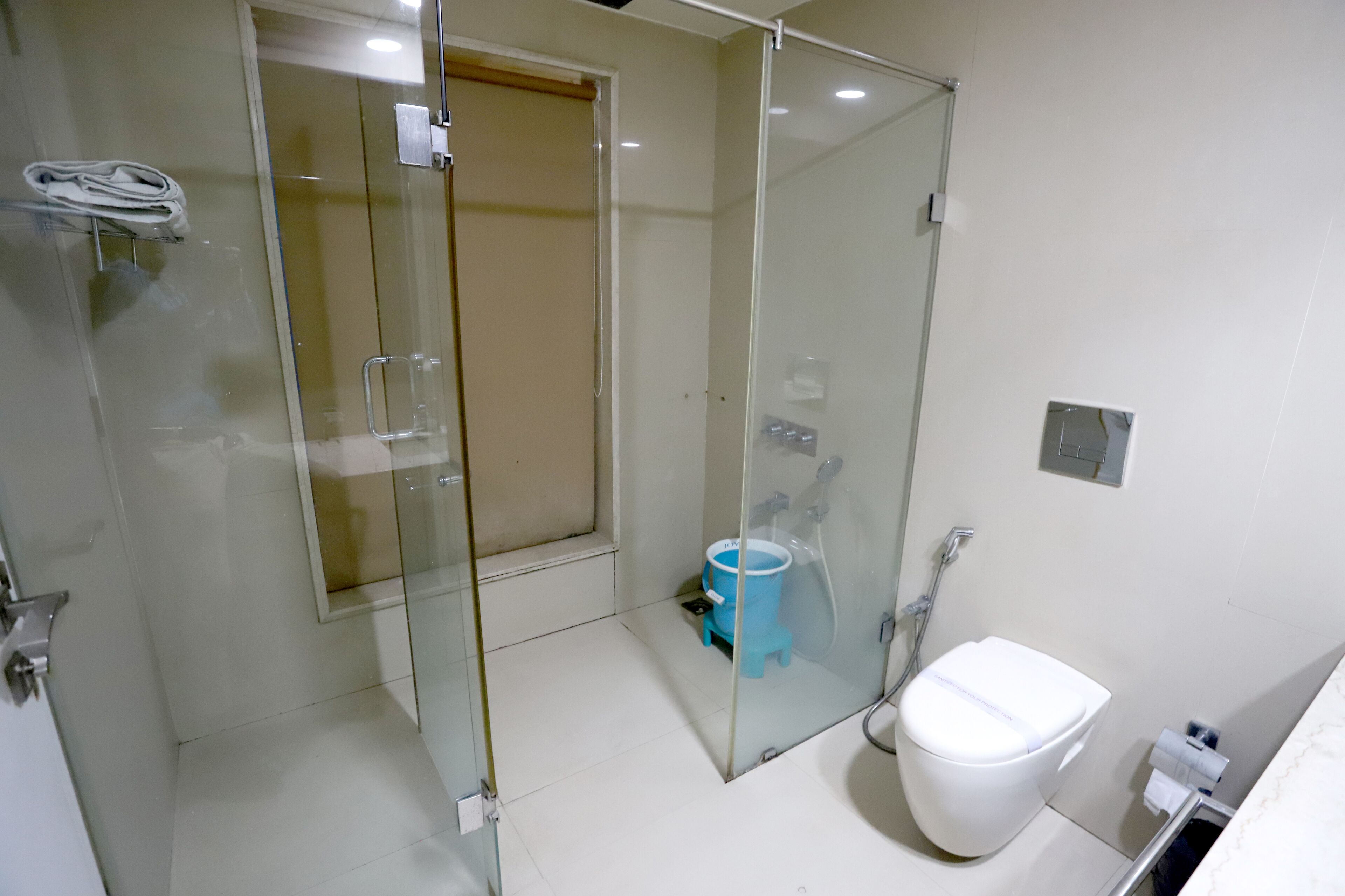 A modern bathroom with a glass shower enclosure, a white toilet, and a blue bucket.