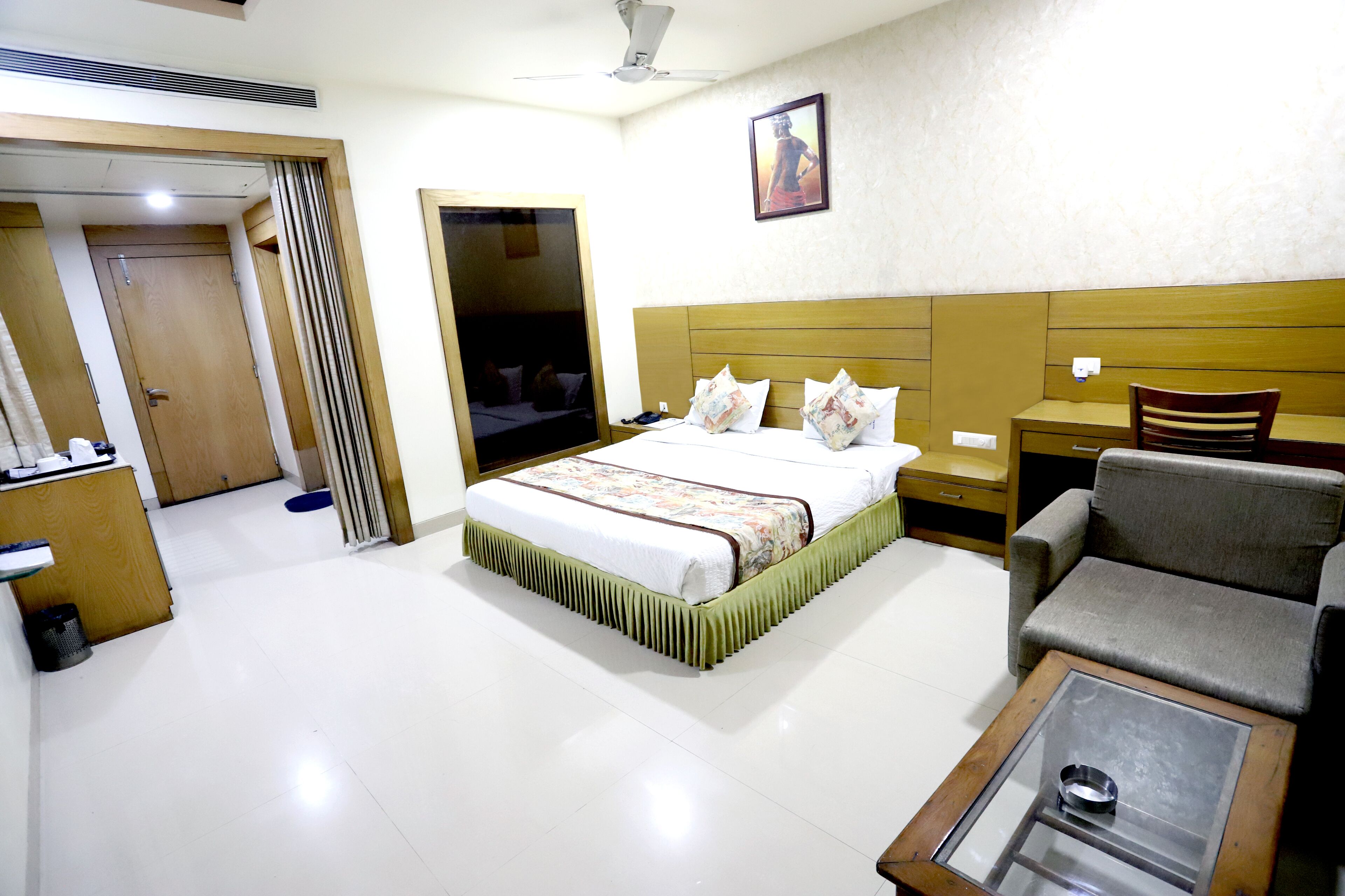 Quarto de hotel com cama, sofá, mesa de centro, cadeira, escrivaninha e guarda-roupa.