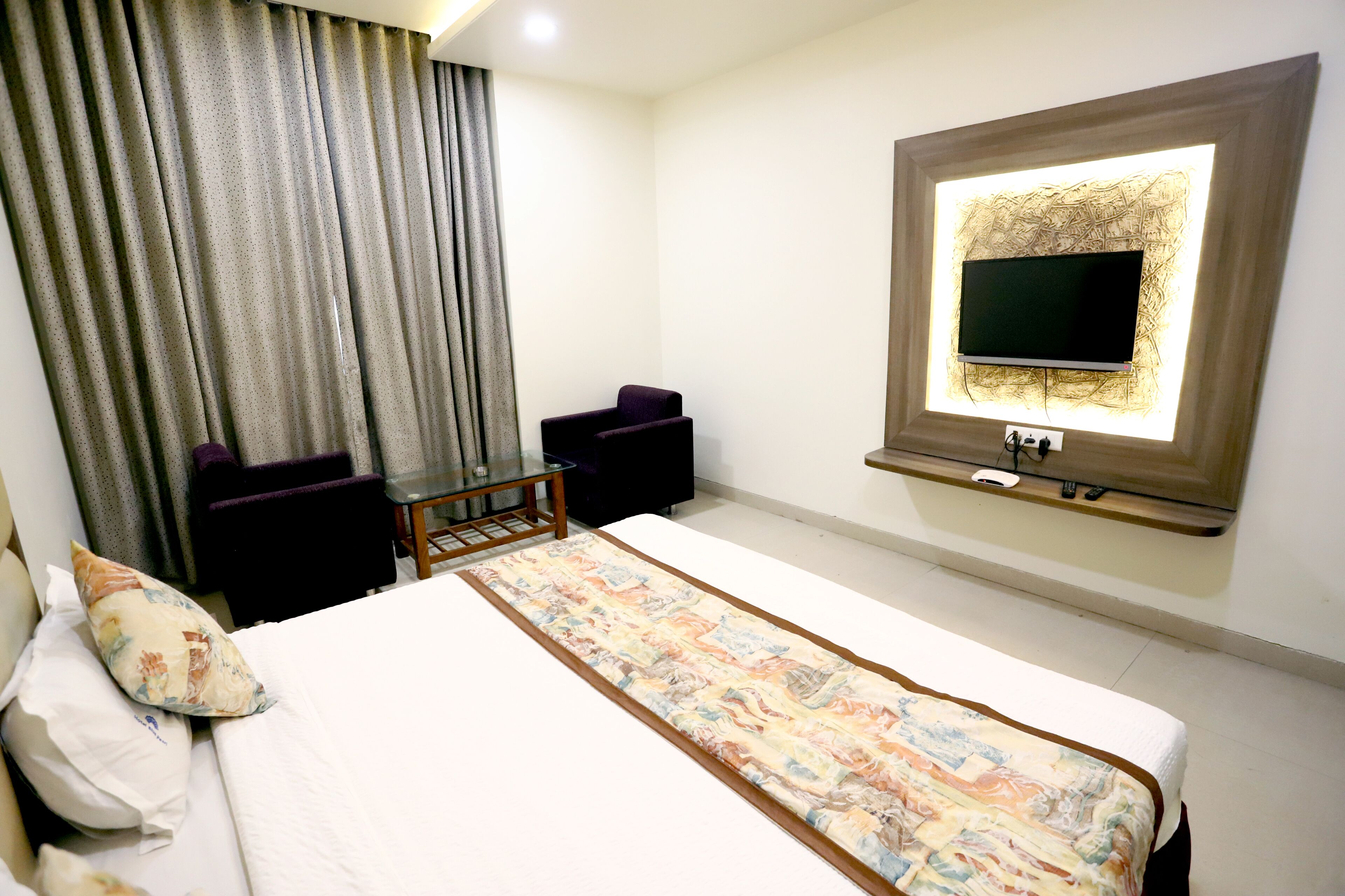 A hotel room with a bed, a TV mounted on the wall, a desk, and a chair.
