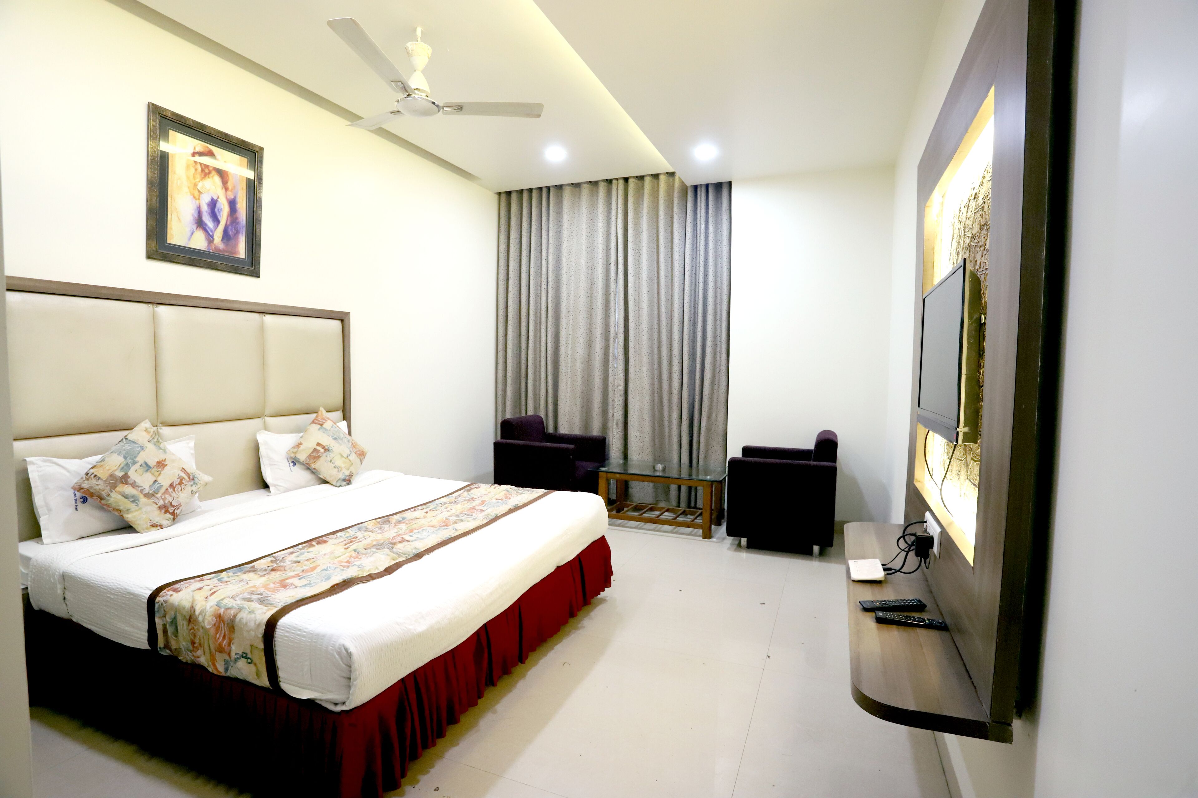 A hotel room with a bed, a ceiling fan, a TV, and a window with curtains.