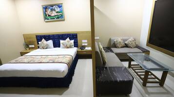 A hotel room with a bed, a sofa, a small table, and a wall-mounted TV.