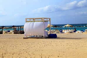 Une plage avec un lit à baldaquin blanc, des chaises longues et des parasols.