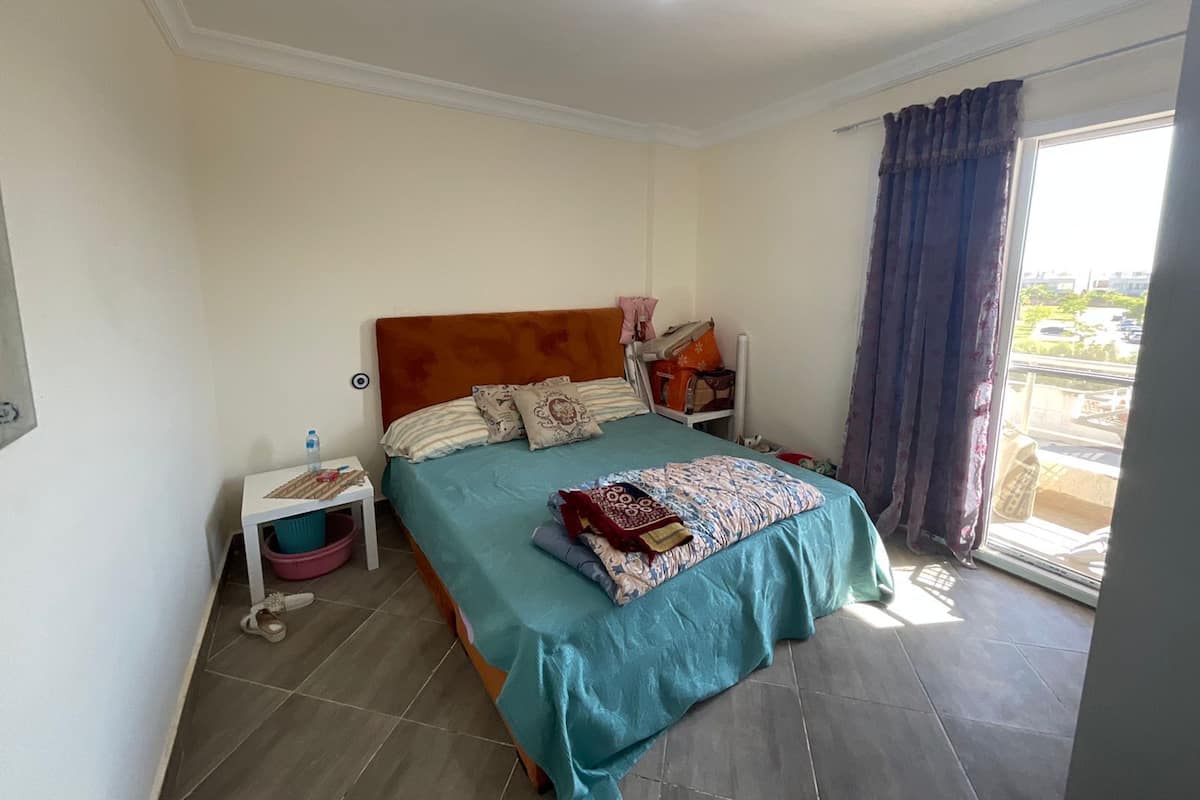 Un dormitorio con cama, mesita de noche, ventana con cortinas y vistas al exterior.