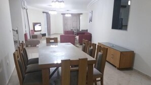 Un comedor amplio con una larga mesa de madera y numerosas sillas, un aparador de madera y un televisor al fondo.