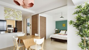 A modern kitchen with a wooden table and white chairs, a bed with a green checkered headboard, and a large potted plant. - Crystal Exe Nippombashi 406 (Osaka)