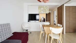 A modern living room with a wooden dining table, white chairs, a red sofa, a flat-screen TV, and a kitchen area with a coffee machine. - Crystal Exe Nippombashi 406 (Osaka)