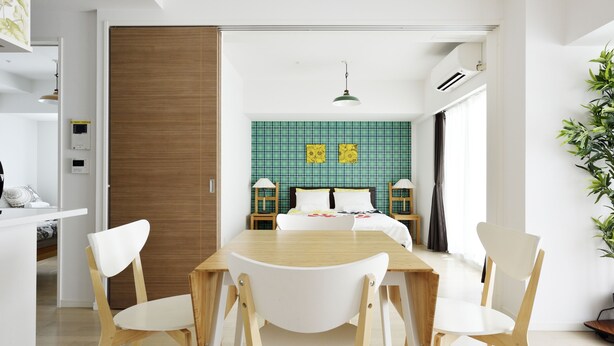 A modern hotel room with a wooden floor, a bed with a green and yellow patterned headboard, a dining table with white chairs, and a large window with curtains. - Crystal Exe Nippombashi 406 (Osaka)