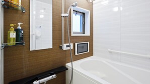 A modern bathroom with a bathtub, a shower, and a small window. There are shelves with toiletries and a towel rack. - Crystal Exe Nippombashi 406 (Osaka)