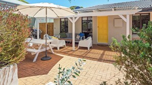 Un patio techado con mobiliario exterior, una parrilla y una puerta amarilla.