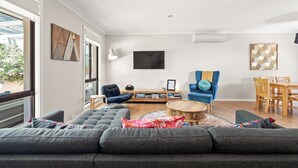 Una sala de estar moderna con un sofá seccional gris, un sillón azul, una mesa de centro de madera y una mesa de comedor con sillas.