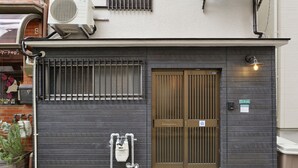 A building with a dark facade, a brown double door, and a small window with bars. - Konpeito House (Osaka)