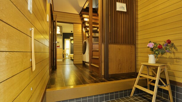 A wooden interior hallway with a tiled floor, a wooden bench, and a small stool with a vase of flowers. - Konpeito House (Osaka)