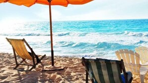 A beach scene with two beach chairs and a large umbrella. - Marseilia Beach 3 (Al-Hammam)