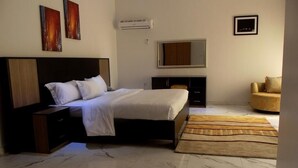 A bedroom with a bed, nightstands, a dresser, a mirror, a sofa, and a rug. - Channel View Hotel (Calabar)