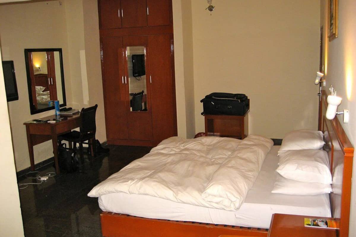 A hotel room with a bed, a desk, a chair, a wardrobe, and a suitcase on the floor.