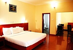A hotel room with a large bed, a desk, and a chair. There is a door leading to a bathroom.