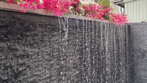 A stone wall with a waterfall feature and pink flowering plants. - Champ de Roses Hotel (Hualien City)