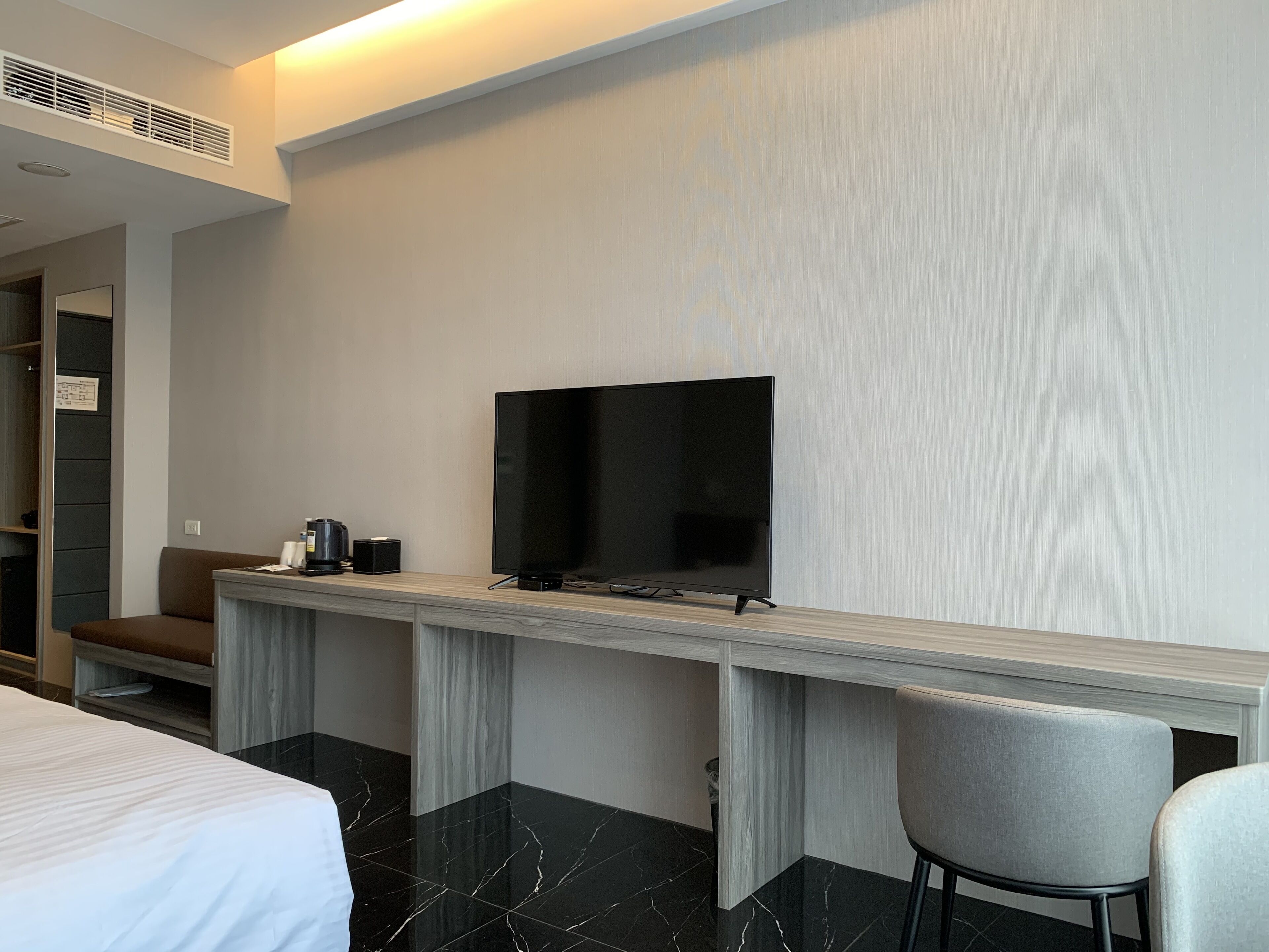 Een hotelkamer met een bed, een bureau met een flatscreen televisie, een stoel en een kleine tafel met een koffiezetapparaat.