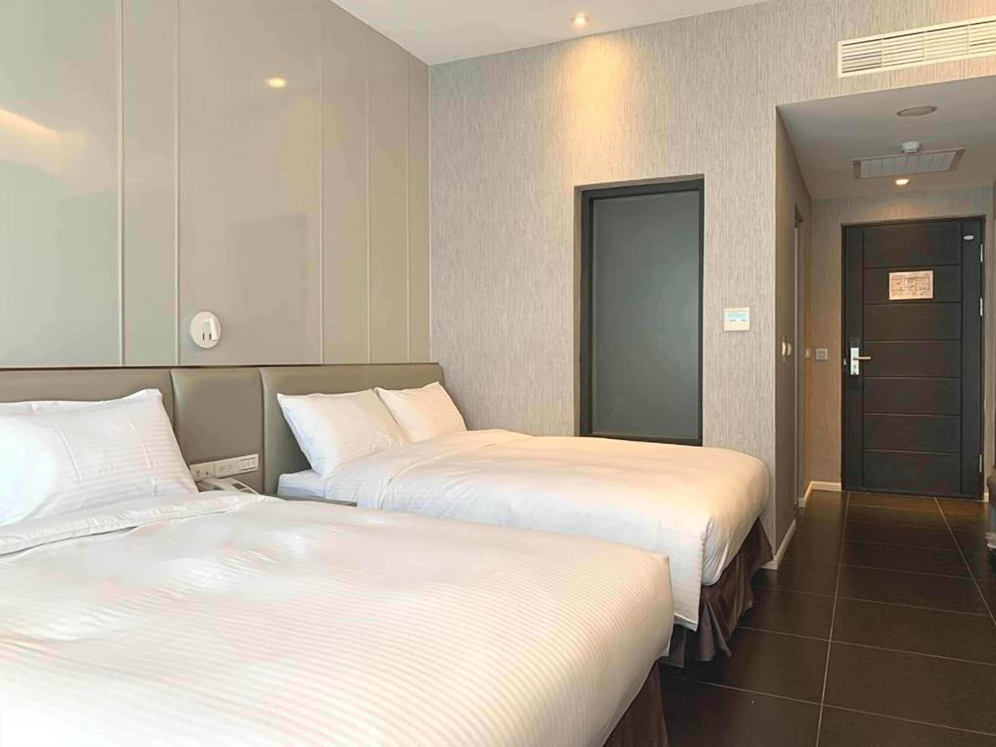 A hotel room with two beds, a door, and a tiled floor.