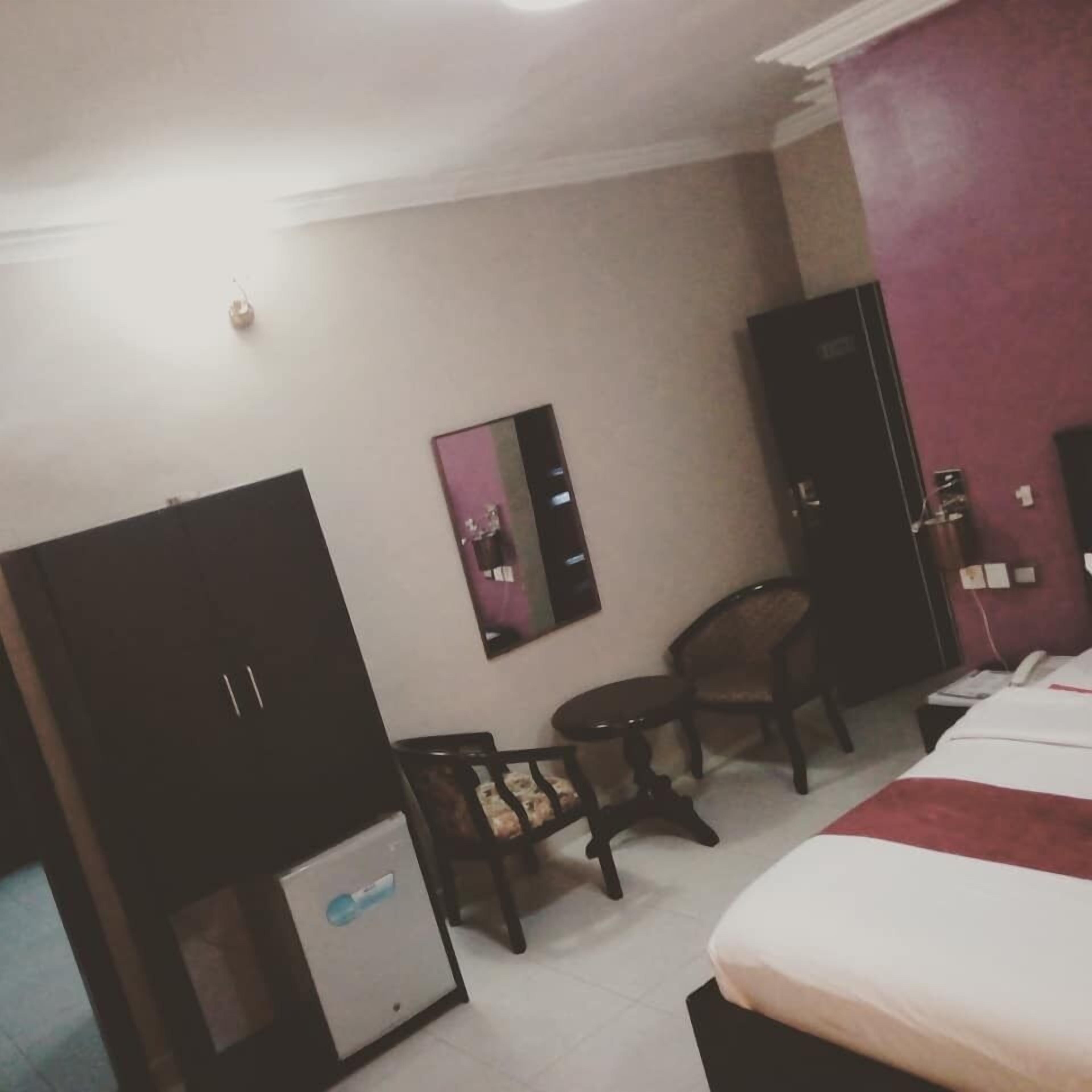 A hotel room with a bed, a desk, a chair, a wardrobe, and a small table.