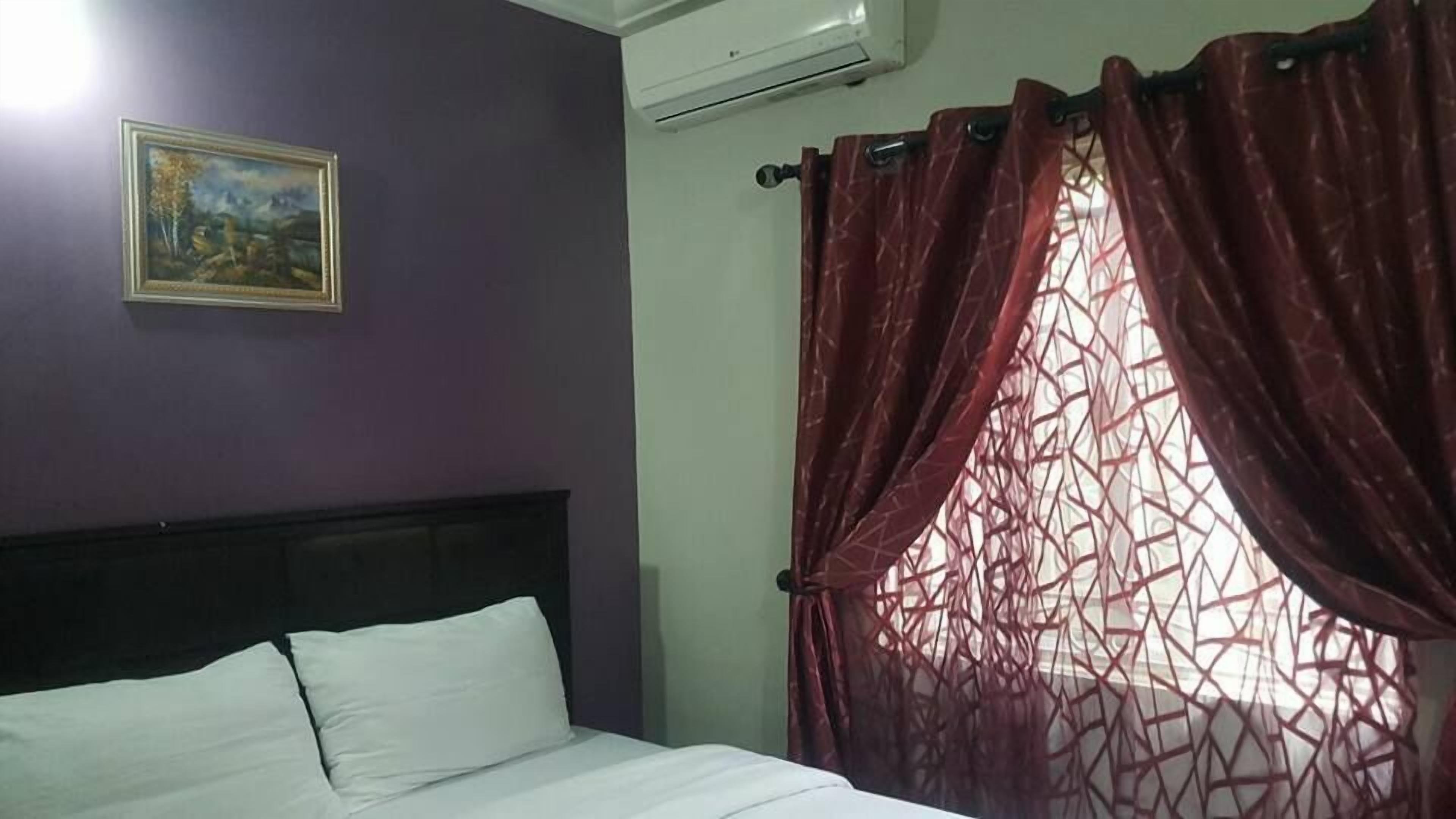 Una habitación con una cama, un cuadro en la pared y una ventana con cortinas rojas.